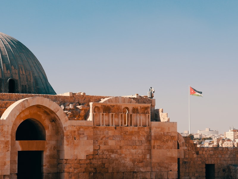 Stone arches of the Umayyad Palace at the Amman Citadel, with the Jordanian flag behind.